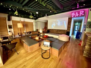 Uma área de estar moderna com bar, sofás e uma tela de projeção.