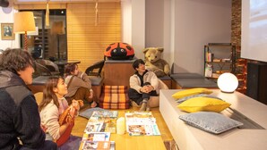 Ein gemütlicher Innenraum, in dem eine Gruppe von Personen an einem Tisch mit Zeitschriften und einem Teddybären sitzt.
