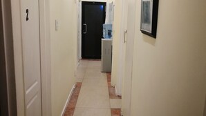 A narrow hallway with white walls, a tiled floor, and doors numbered 2 and 3. A water dispenser is visible on the right wall. - Luc Lodge (Cape Town)