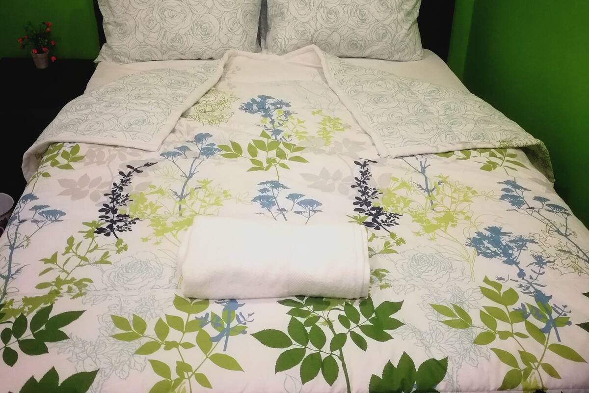 A bed with a floral bedspread and two pillows, set against a green wall.