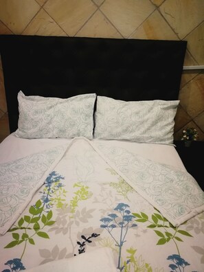 A bed with a black headboard, white pillows with a rose pattern, and a floral bedspread with green and blue flowers.