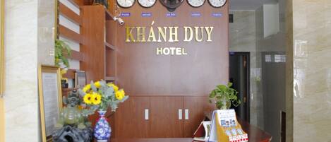 A reception desk with clocks, a wooden panel, and a sign that reads "KHÃNH DUY HOTEL".