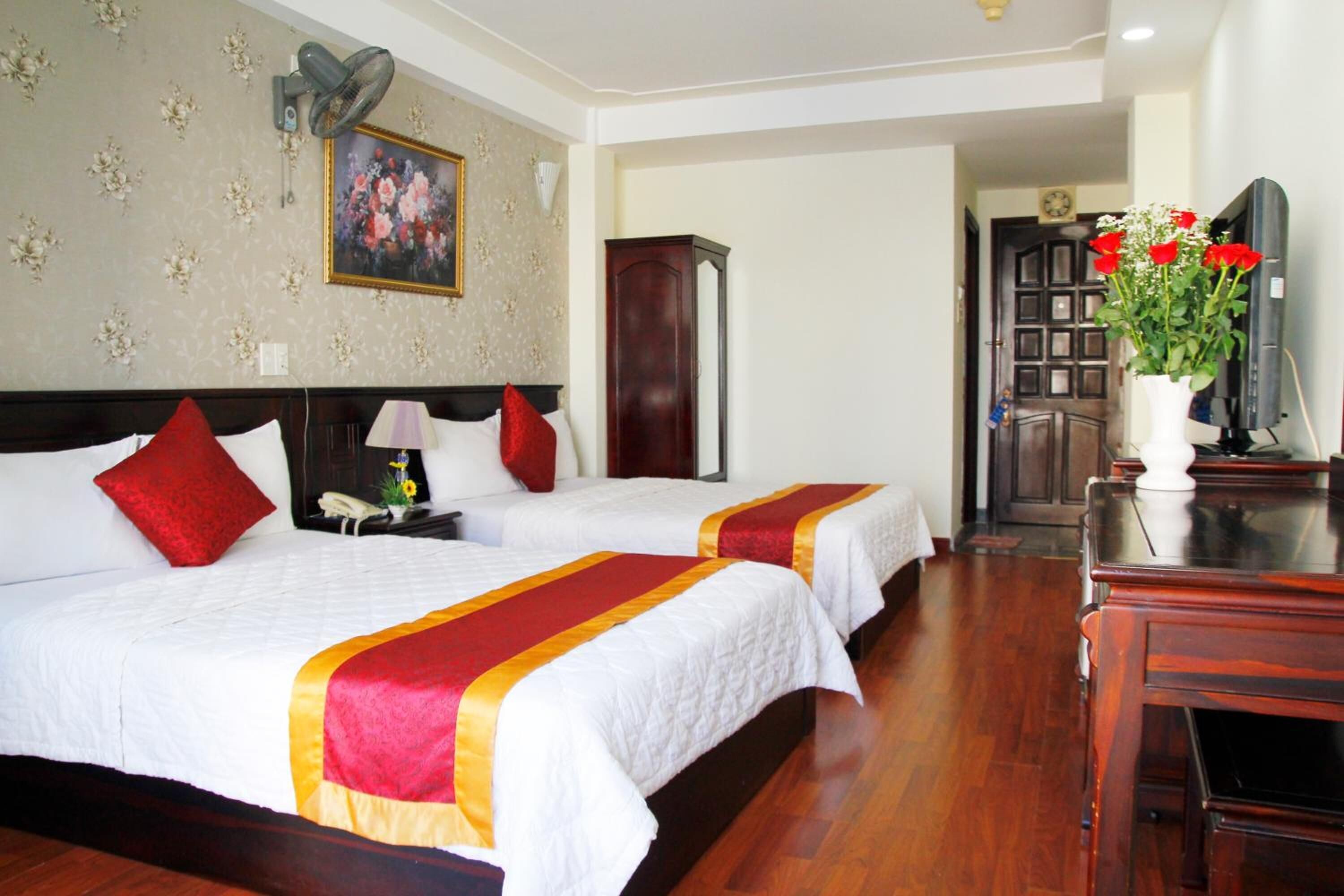 A hotel room with two beds, a wooden dresser, a TV, and a floral painting on the wall.