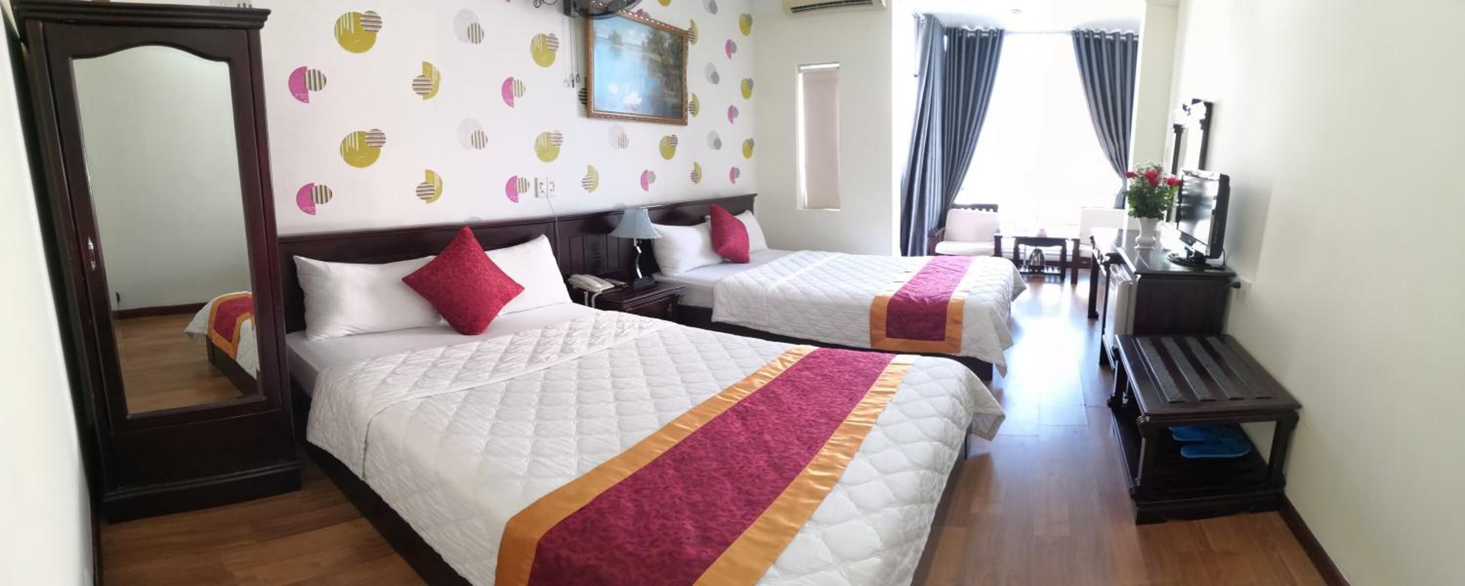 A hotel room with two beds, a wooden floor, a mirror, a desk with a chair, and a piano.