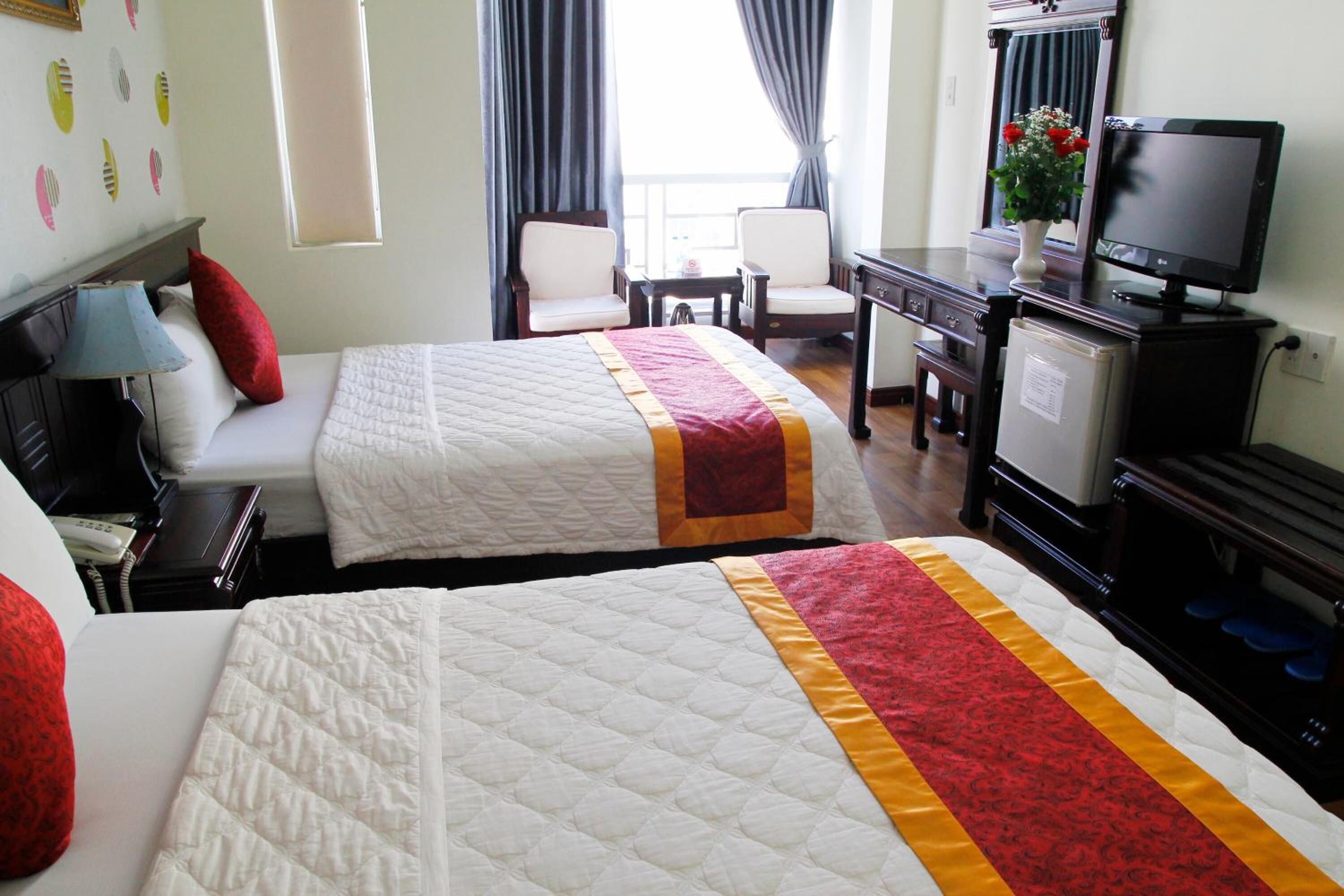 A hotel room with two beds, a desk with a computer, a TV, and a small refrigerator.