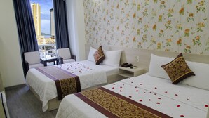 A hotel room with two beds, a small table, and a view of a cityscape. - Khanh Duy Hotel (Nha Trang)