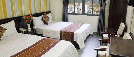 A hotel room with two beds, a desk, and a chair. There is a window with a view of buildings and mountains.