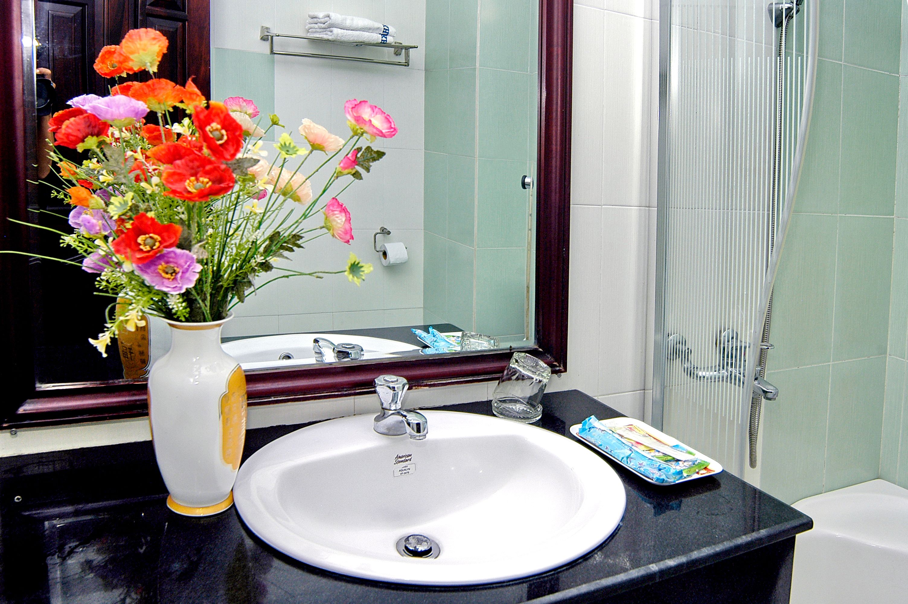 A bathroom with a white sink, a mirror, a vase with flowers, and a shower area.