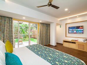 A hotel room with a bed, a TV, a ceiling fan, and a view of the outdoors.