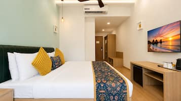 Habitación de hotel con cama, escritorio, ventilador de techo, aire acondicionado, un cuadro y una puerta que da a otra habitación.