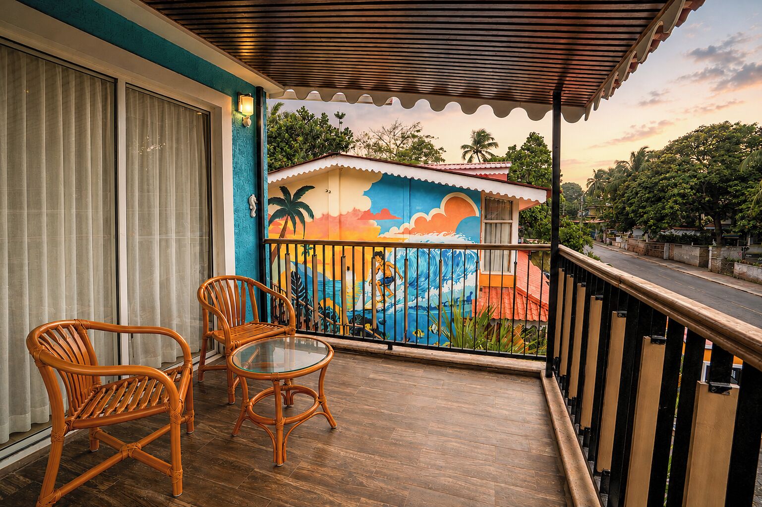 Uma varanda com cadeiras de vime, uma mesa de vidro e um mural colorido com tema tropical.