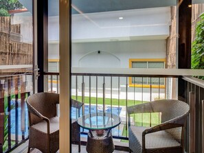 Un balcón con sillas de mimbre, una mesa de vidrio y vista a una piscina.
