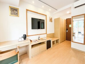 Une chambre d’hôtel avec un bureau en bois, une télévision, un lit et une porte coulissante donnant sur un balcon.
