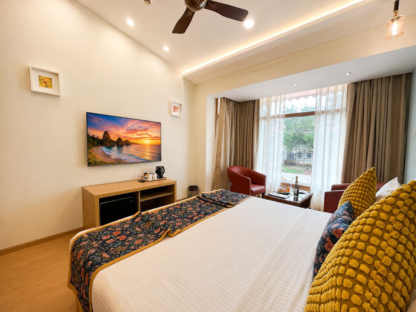 Habitación de hotel con cama, escritorio, silla, televisión y ventana con cortinas.