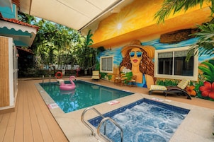 An indoor swimming pool with a mural, a hot tub, and lounge chairs.