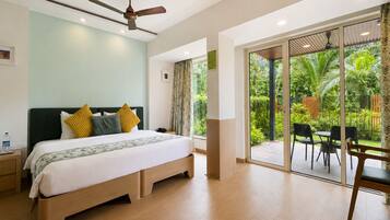 Una habitación de hotel moderna con una cama grande, ventilador de techo y puerta corrediza de vidrio que da a un jardín con mobiliario exterior.