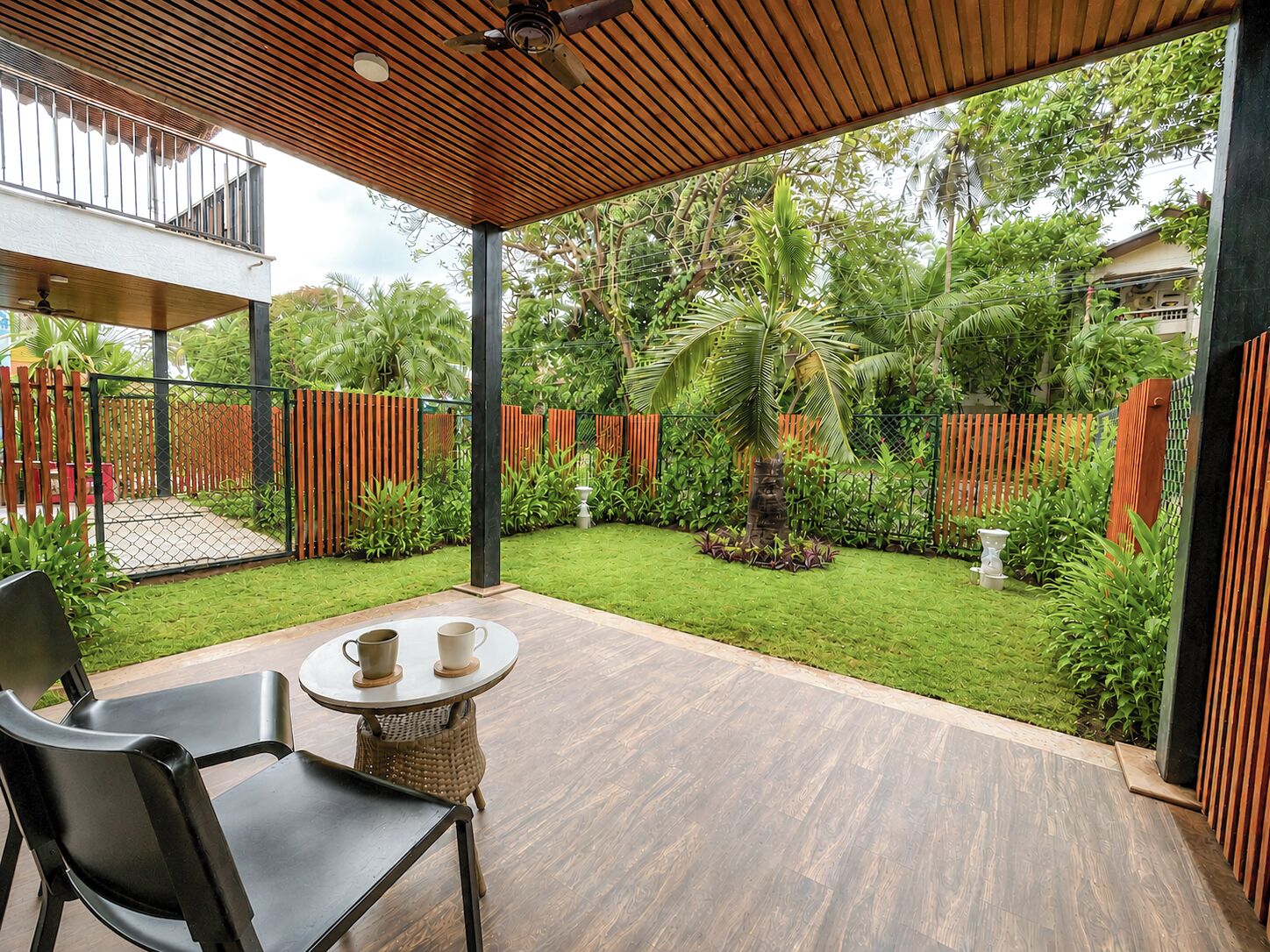 Ein überdachter Patio-Bereich mit Tisch und Stühlen, umgeben von einem üppigen Garten und einem Holzzaun.