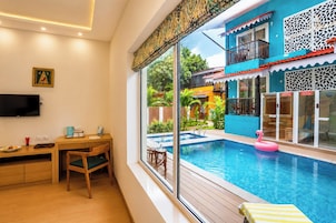 Habitación con una ventana grande que da a una piscina, un escritorio de madera, un televisor y una mesita con una taza y un plato.