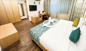 A hotel room with a bed, a desk, a chair, a TV, and a wardrobe.