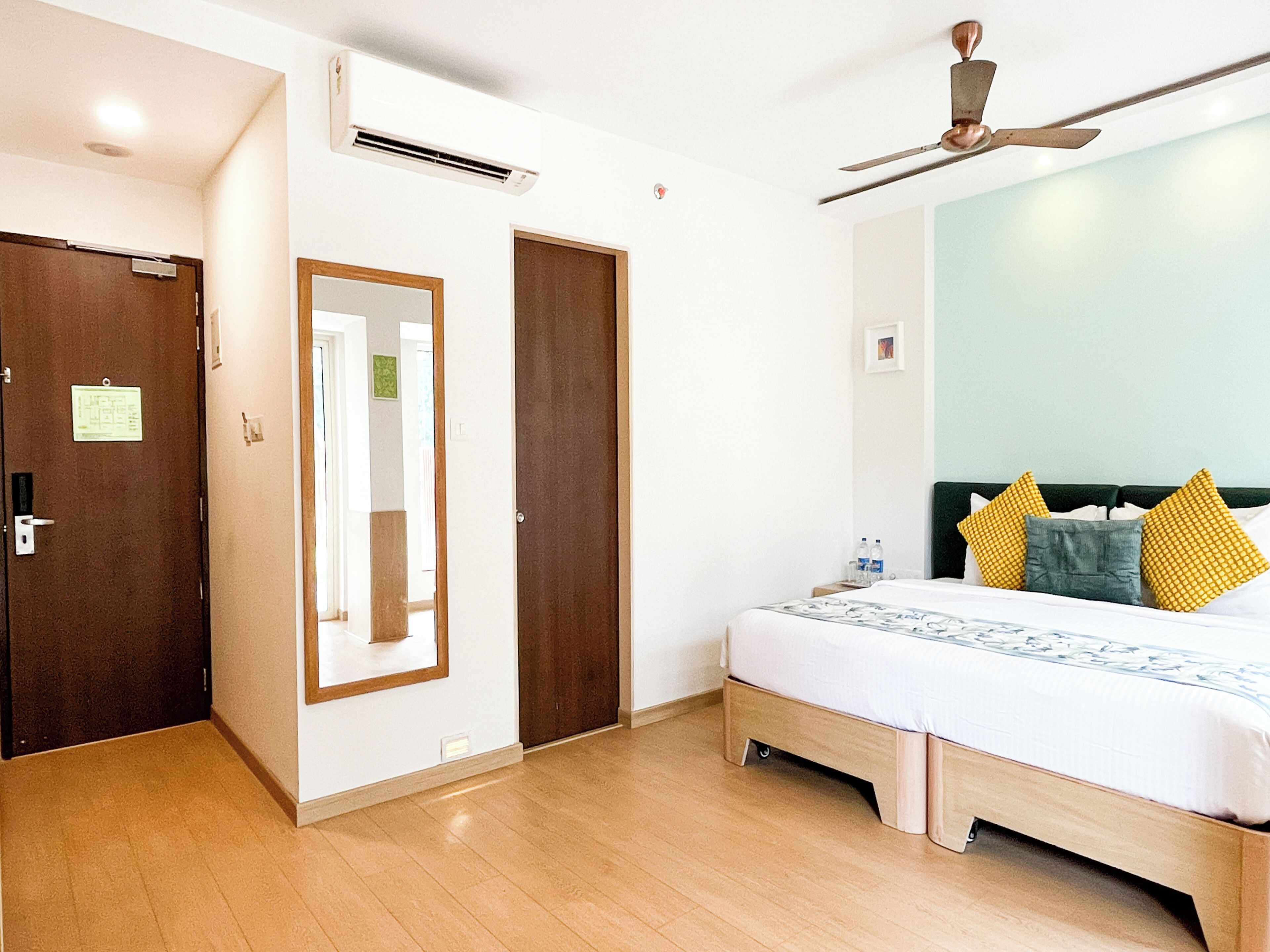 A hotel room with a bed, a ceiling fan, an air conditioning unit, and a door with a mirror.