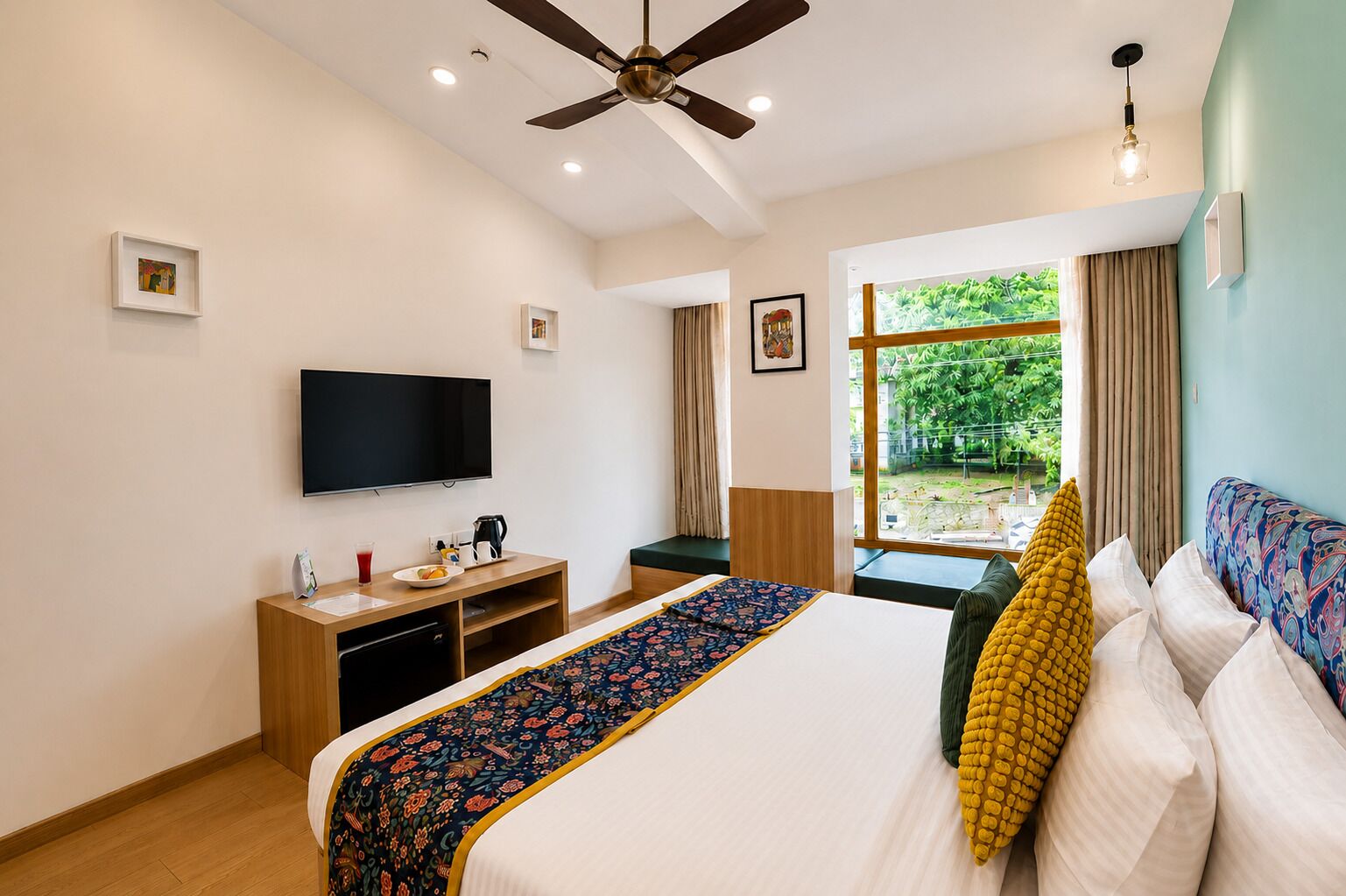 Une chambre d’hôtel équipée d’un lit, d’un bureau avec un téléviseur à écran plat, d’un ventilateur de plafond et d’une fenêtre donnant sur un paysage verdoyant.