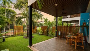 A covered patio area with a wooden floor, a table with chairs, and a view of a residential building in the background. - The BeachWalk Resort by Acron (Candolim)