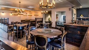 Un restaurante con mesas redondas, sillas de madera oscura y varios candelabros colgantes.
