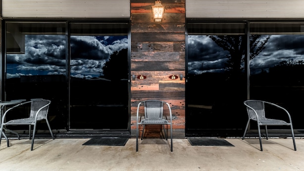 Un edificio moderno con amplias puertas de vidrio, dos sillas de metal y una pared de madera decorativa con una lámpara.