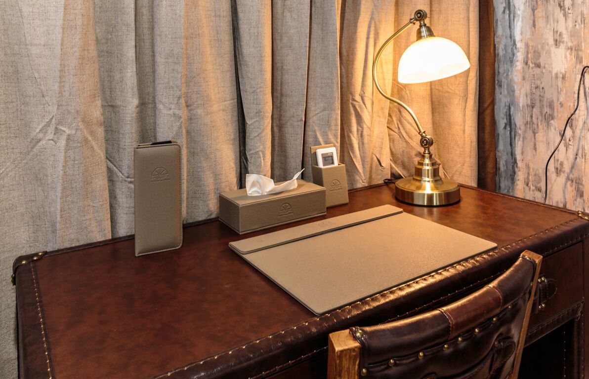 A wooden desk with a leather chair, a lamp, a tissue box, and a box with a picture frame.