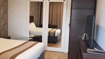 A modern hotel room with a large bed, a wardrobe with mirrors, a desk with a computer, and a television.