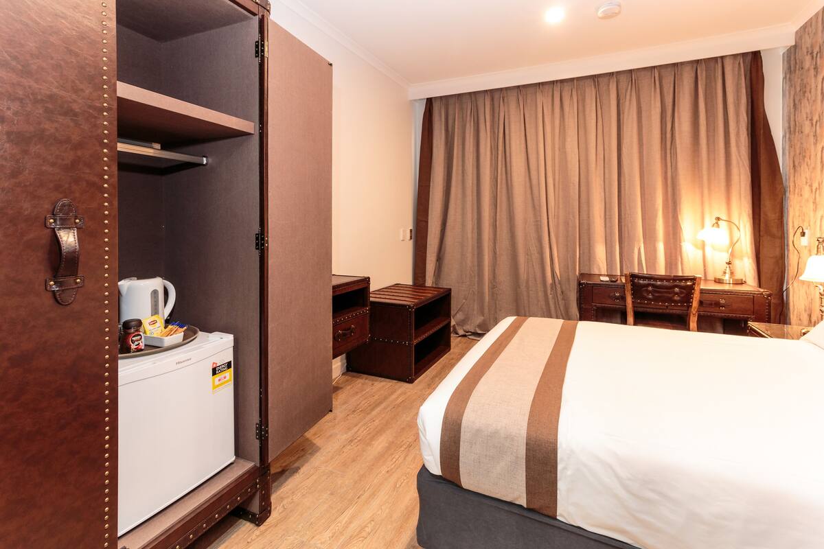 A hotel room with a bed, a wardrobe, a desk, and a nightstand.