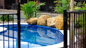 Una piscina con revestimiento azul, rodeada por una valla metálica y diversas plantas.