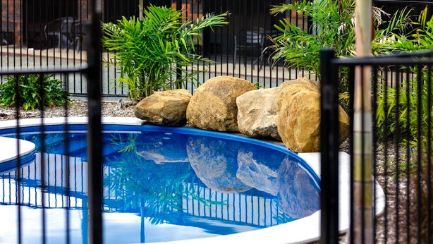 A swimming pool with a blue interior, surrounded by a metal fence and various plants.