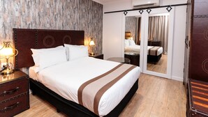 Una habitación de hotel con una cama grande, un armario, un espejo y una mesita de noche con lámpara.