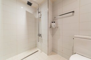 A modern bathroom with a glass-enclosed shower, a toilet, and a shelf with toiletries. - Cogora Hotel (Incheon)