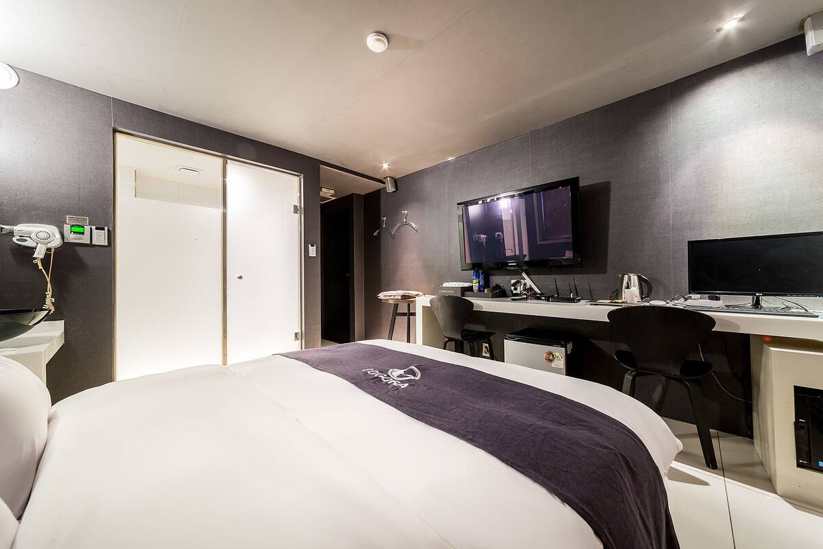 A modern hotel room with a bed, desk, and television.