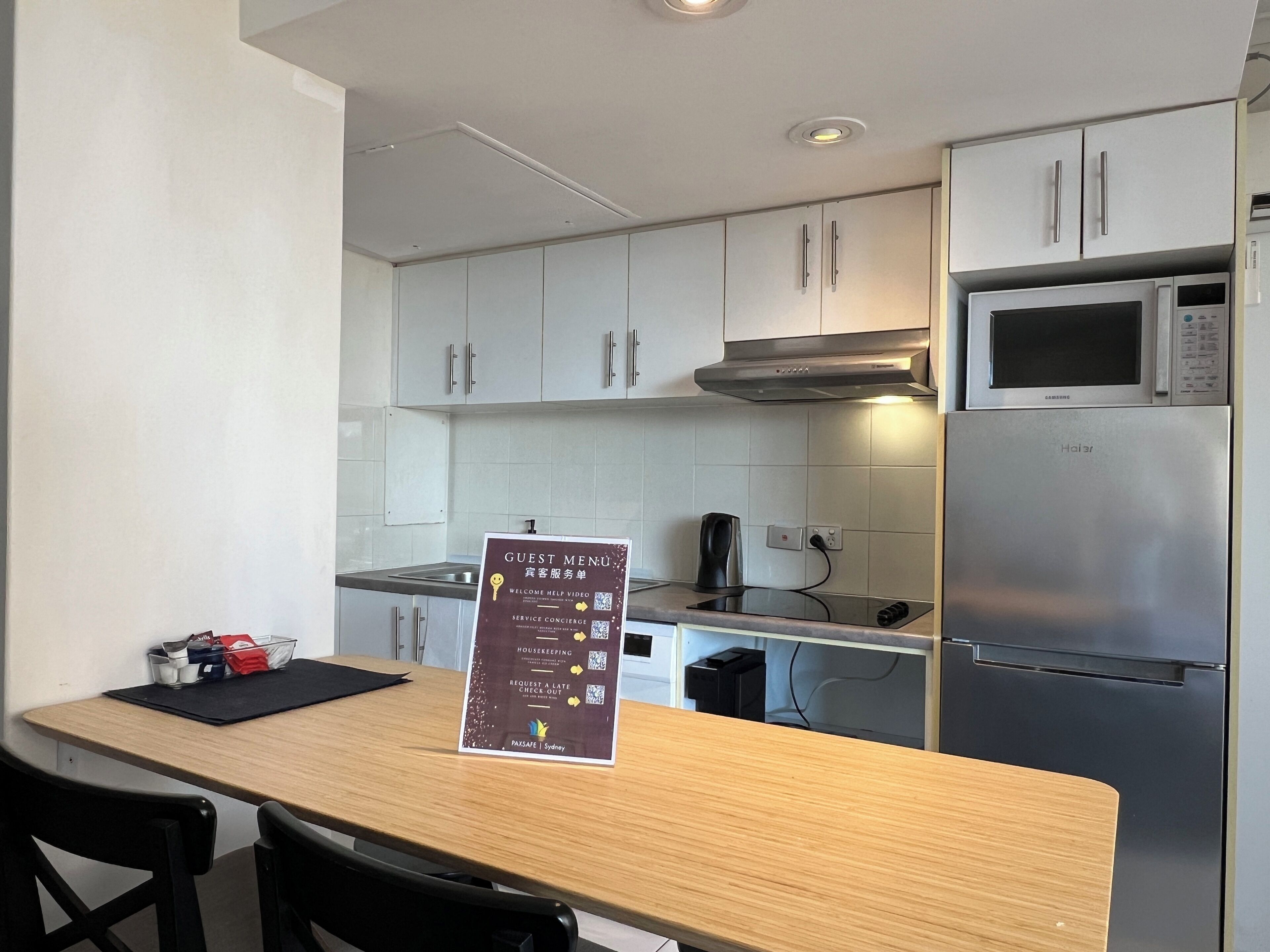 A modern kitchen with stainless steel appliances, a wooden table, and a sign detailing guest services.