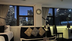 A modern hotel room with a sofa, a coffee table, and a view of the cityscape at night. - Sydney Hyde Park Paxsafe Apartments (Darlinghurst)