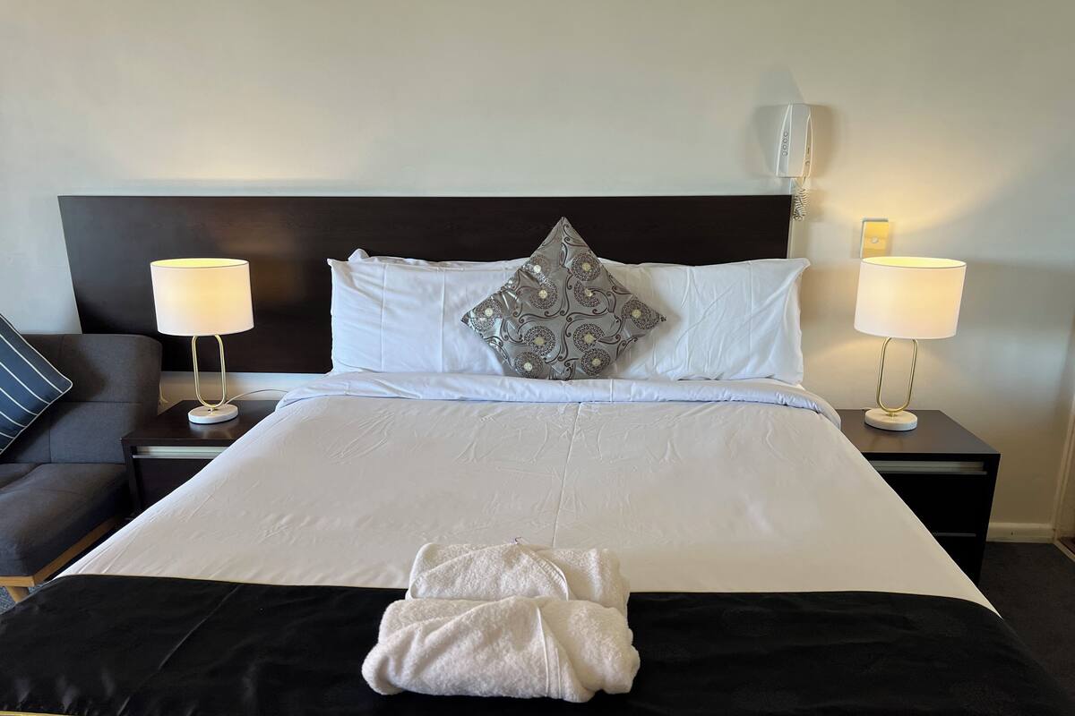 Una cama bien hecha con sábanas blancas, un detalle en negro y dorado, y dos lámparas de noche.