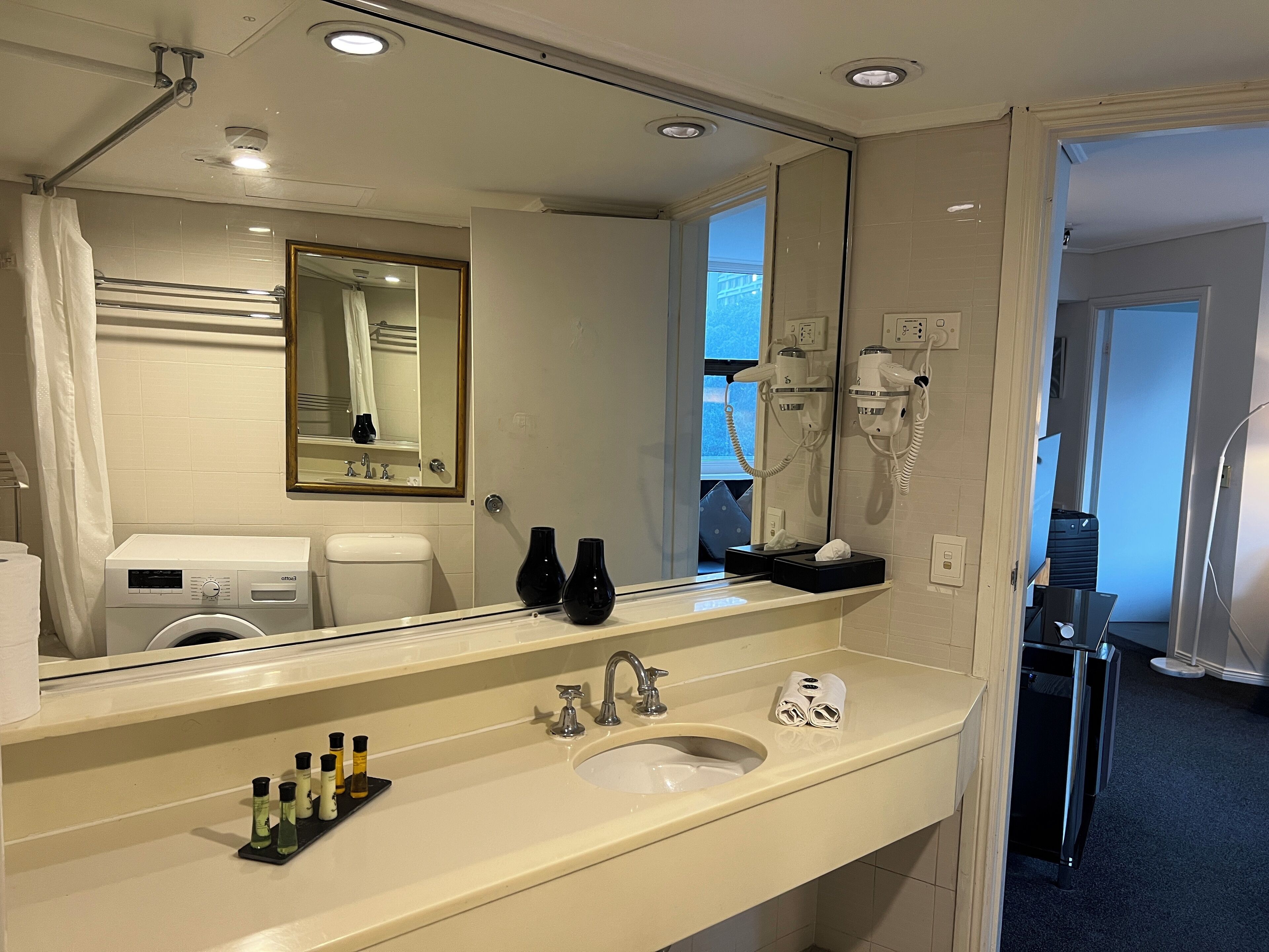 Bagno d'albergo con uno specchio grande, un lavandino, un asciugacapelli e un water.