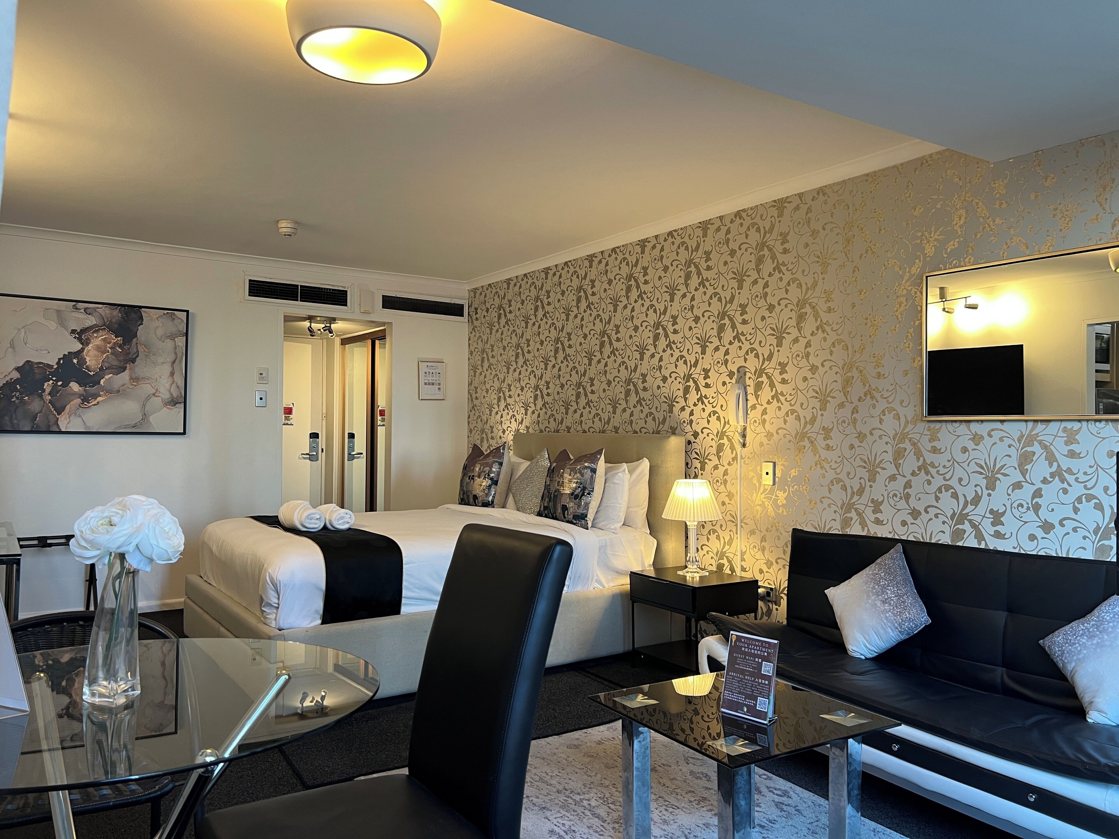 Quarto de hotel com cama, sofá, mesa de vidro e luminária.