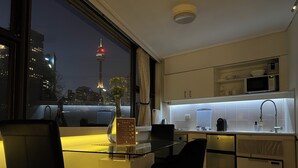 A modern hotel room with a kitchen area, a dining table with chairs, and a view of a cityscape at night. - Sydney Hyde Park Paxsafe Apartments (Darlinghurst)