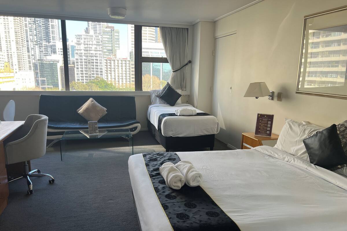 Habitación de hotel con una cama, un escritorio, una silla y vistas a edificios altos.