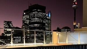 A nighttime view of a cityscape with illuminated buildings and a tower in the background. - Sydney Hyde Park Paxsafe Apartments (Darlinghurst)