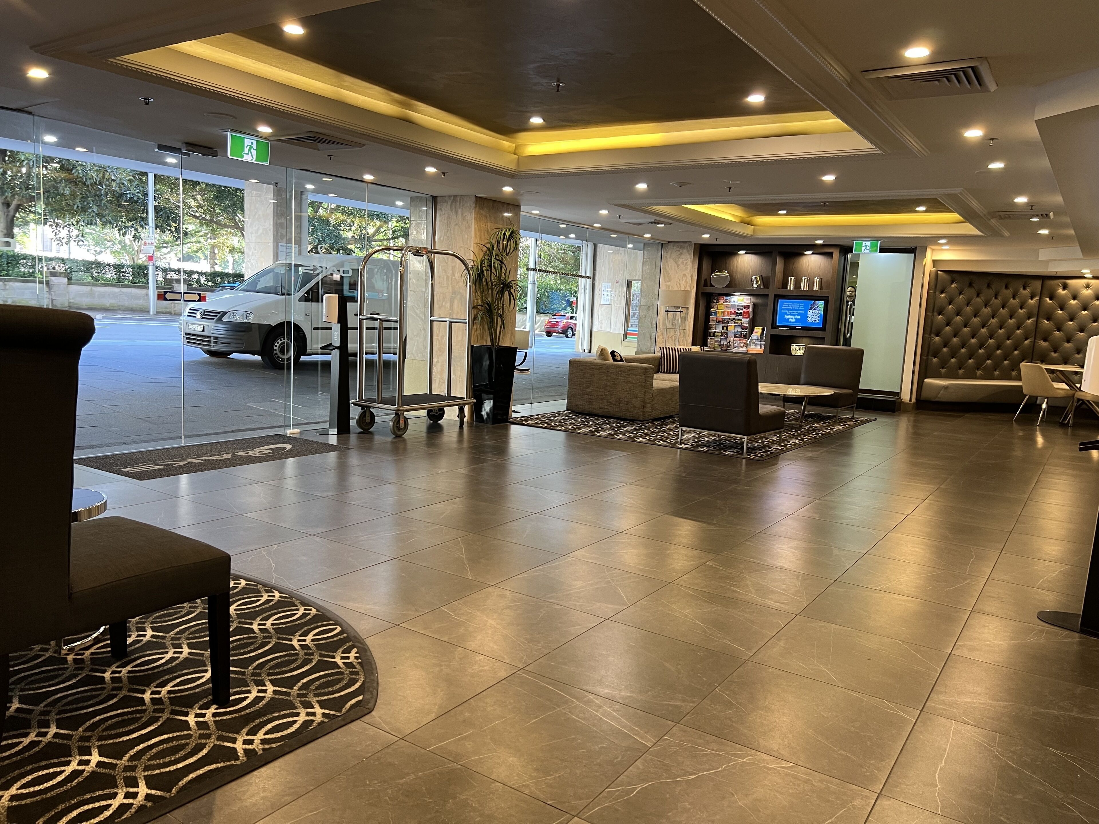 A hotel lobby with a reception desk, seating area, and a large window overlooking the street.