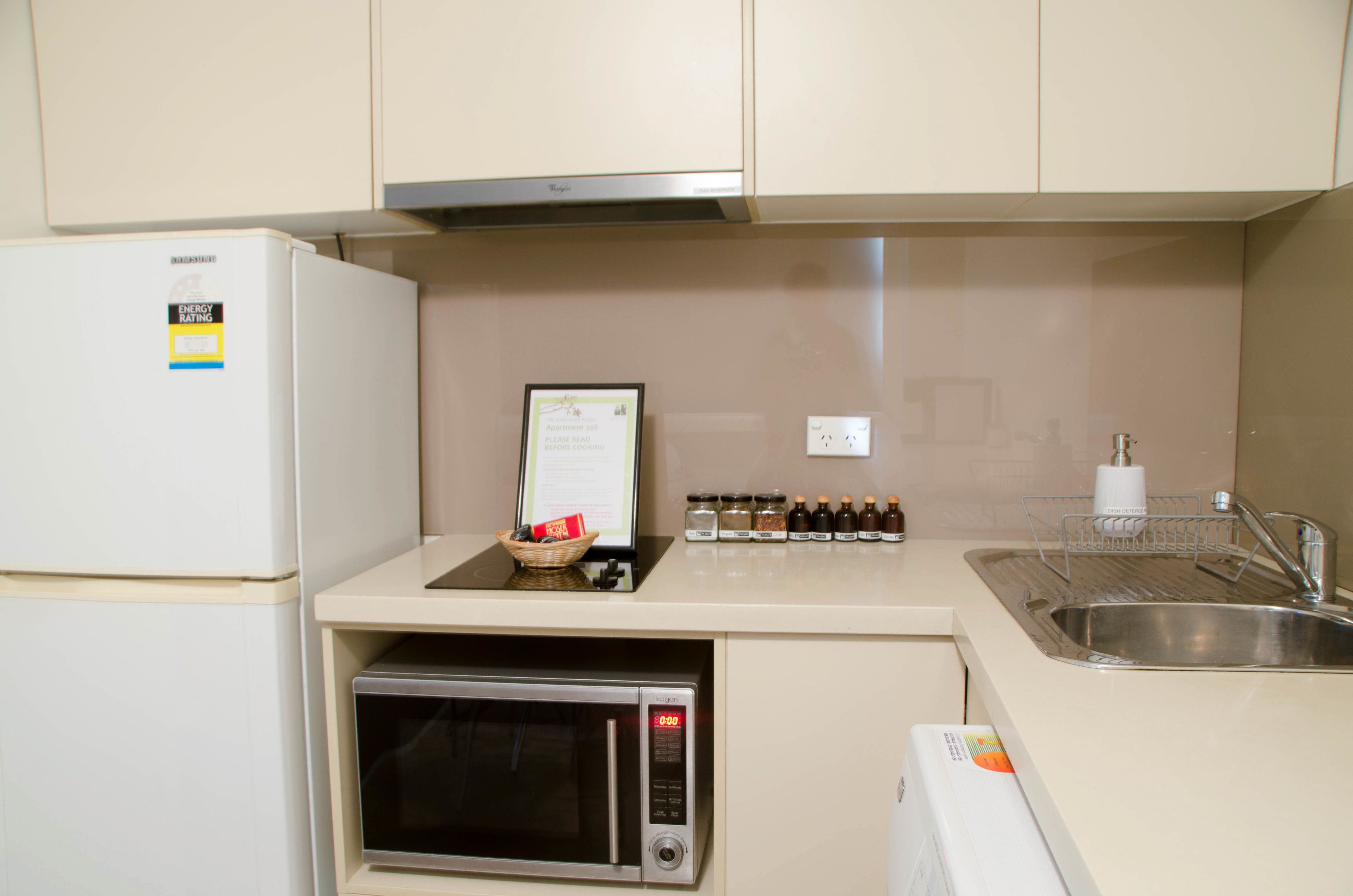 A compact kitchen with a refrigerator, microwave, sink, and a small countertop with jars and a basket.