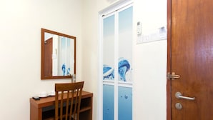 Una habitación pequeña con un escritorio de madera, una silla, un espejo y una puerta con marco azul.