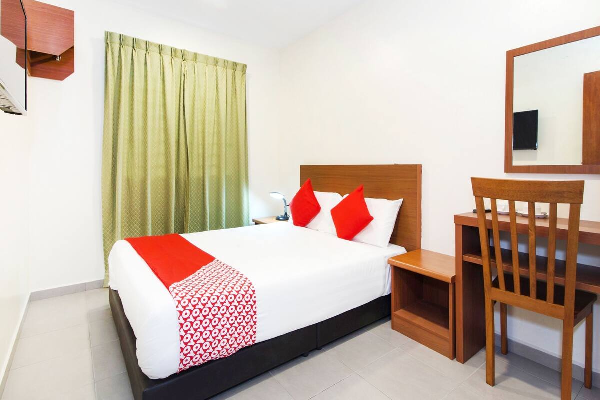 Habitación de hotel con cama, escritorio, silla, espejo y ventana con cortinas.