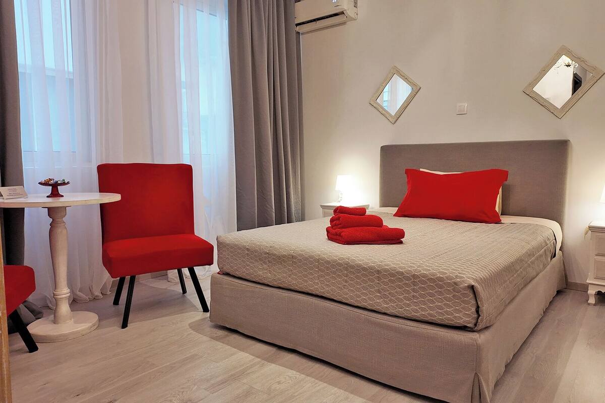 A hotel room with a bed, a chair, a small table, and a nightstand.