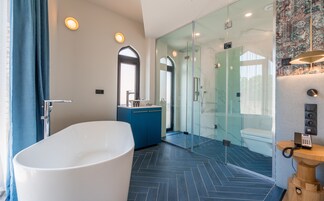 Un baño moderno con una bañera independiente, cabina de ducha de vidrio y un tocador con mueble azul.
